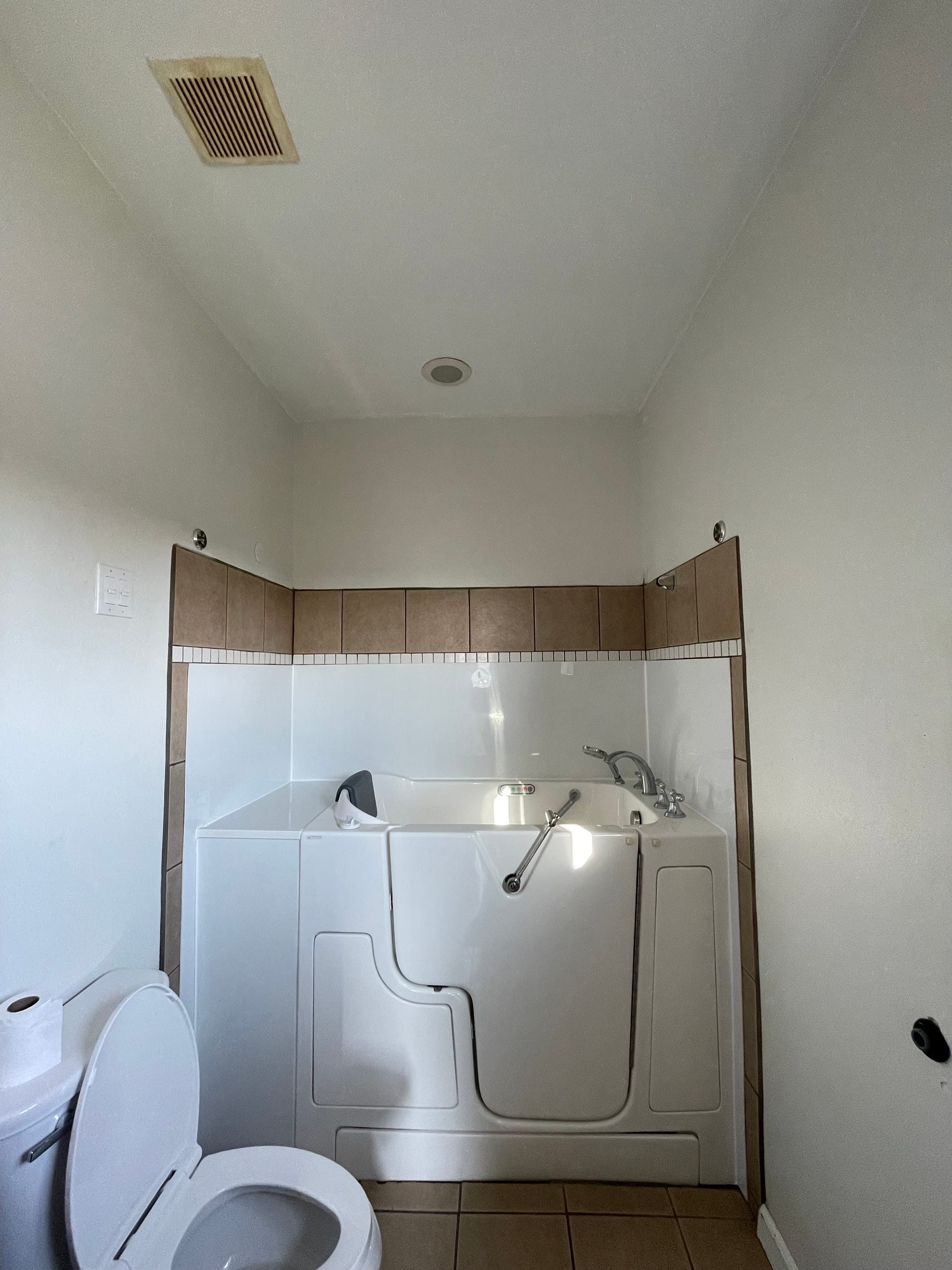 The original bathroom alcove: a high-sided step-in tub against brown tile wainscot, with beige floor tile.