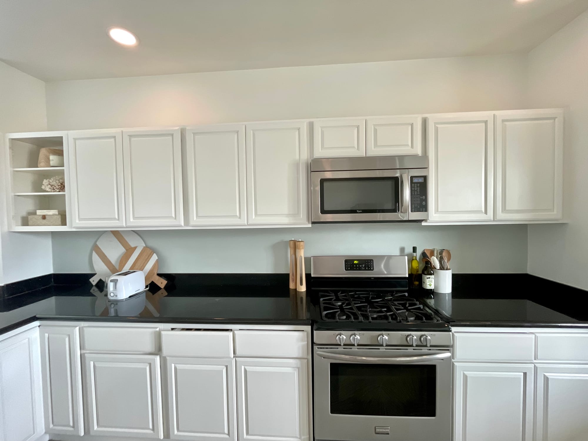 The same run of cabinets with the walls repainted soft white, open shelving added at the end of the run, and a microwave in place of the range hood.