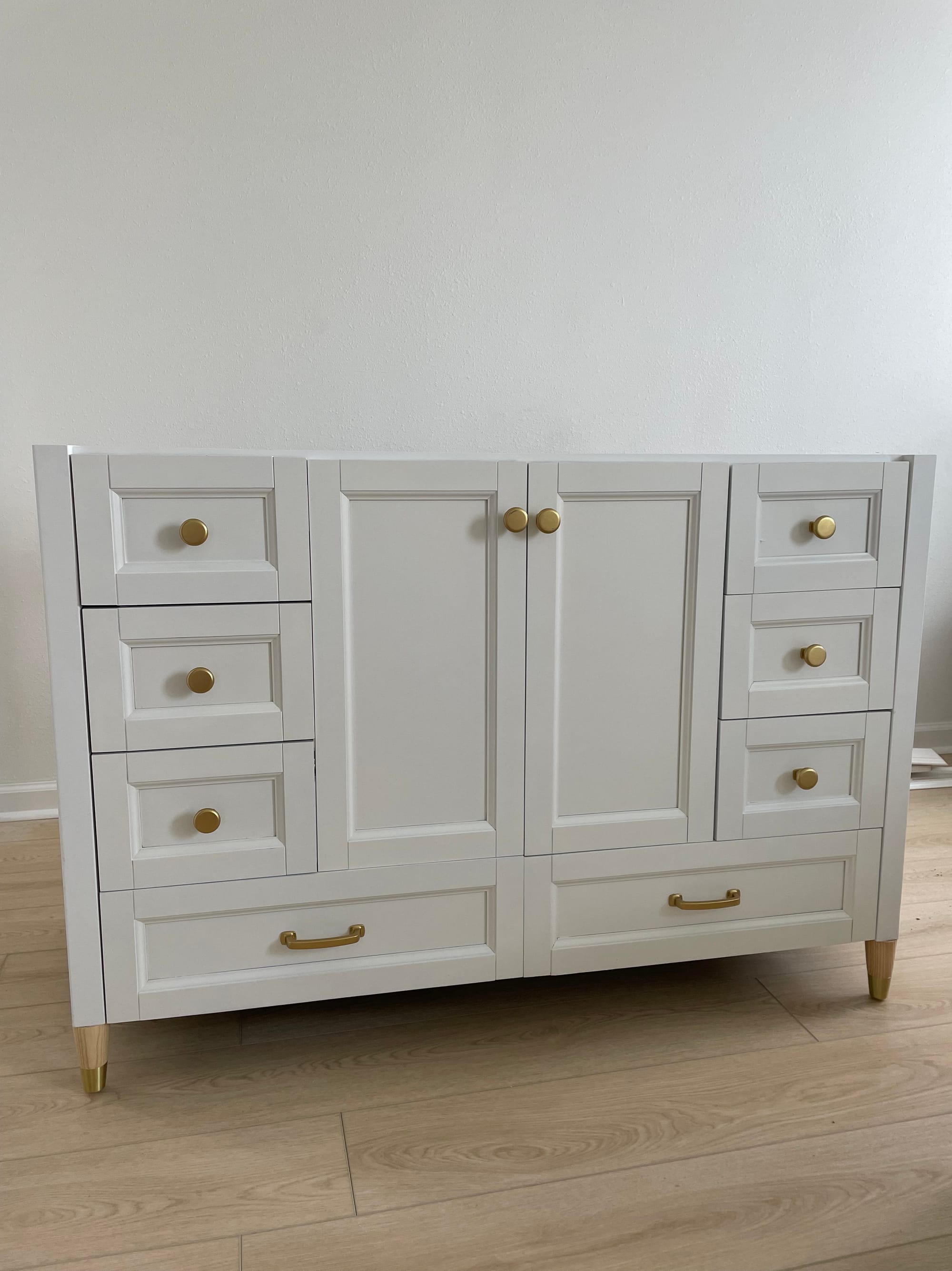 The replacement vanity in warm white, with brass knobs, brass drawer pulls and brass-capped feet.